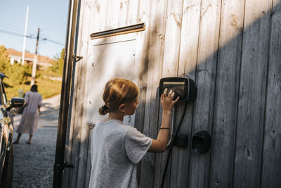 Boy with blond hair operating touch screen car charging device mounted on wooden wall