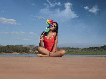 Side view of woman sitting on beach against sky