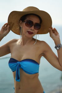 Portrait of woman in sunglasses and hat standing against sea