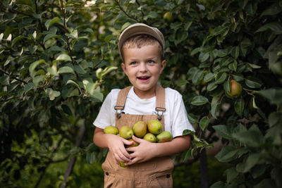 A boy in a cap and beige overalls is harvesting apples. a small farmer works in an orchard