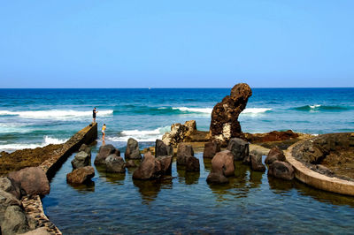 Scenic view of rocks in sea against clear sky