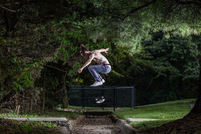 Full length of man doing stunt with skateboard at park 