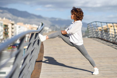 Full length of young woman exercising on bridge during sunny day