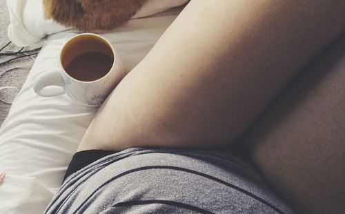 Midsection of woman with coffee lying on bed at home