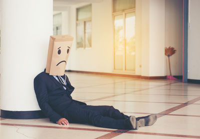 Businessman covering face with paper bag while sitting on floor