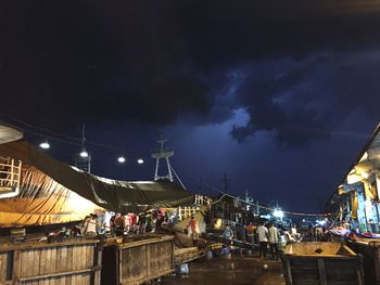 People in illuminated market against sky at night