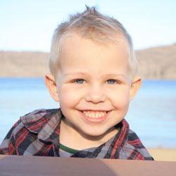 Close-up portrait of smiling boy against lake