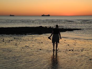 Rear view of silhouette woman walking on beach during sunset