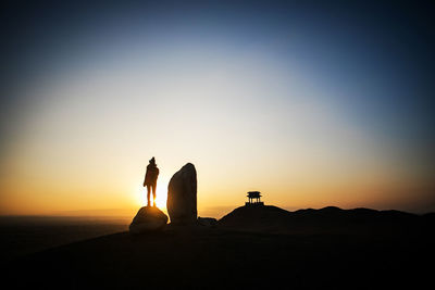 Silhouette man standing on rock against sky during sunset