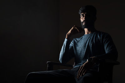 Man looking away while sitting against black background