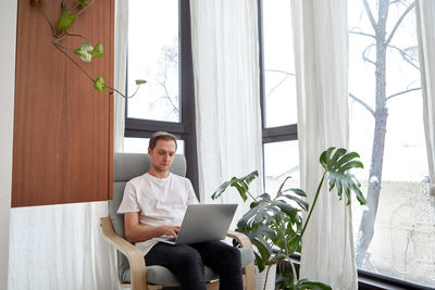 Man working using laptop at home while sitting in chair