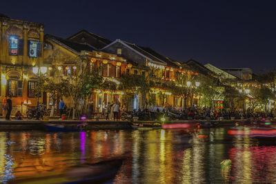 Illuminated buildings by canal against sky at night