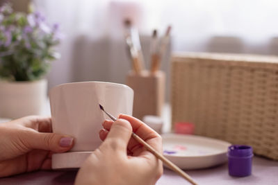 Female paints with a brush, on a white ceramic pot