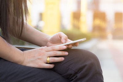 Midsection of woman using mobile phone while sitting on retaining wall