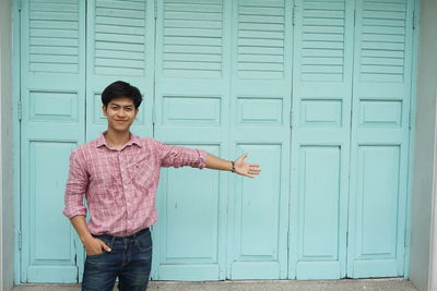 Smiling young man with bag standing against door
