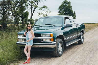 Teen girl leaning against a green truck parked along a dirt road