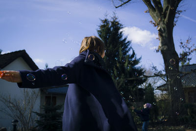 Low angle view of woman standing in yard amidst bubbles against sky