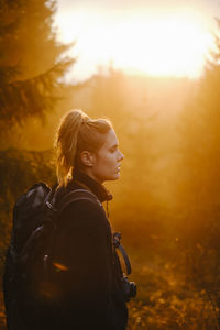 Side view of woman standing in forest during sunset