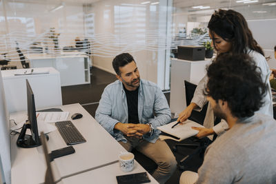 Young businesswoman showing strategy to male colleagues while discussing at office