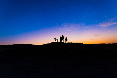 Silhouette people on desert against sky at sunset