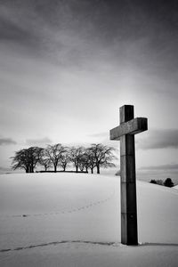 Cross on snow covered landscape against sky