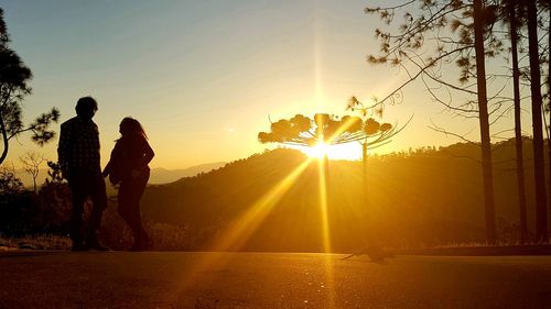 Rear view of silhouette people on landscape against sunset sky