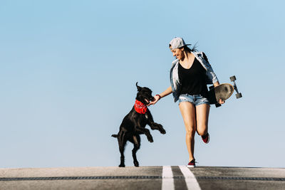 Woman with dog and skateboard against clear blue sky