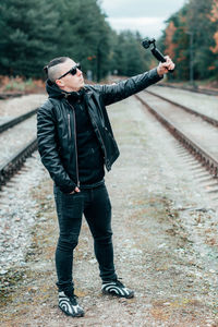 Young man blogging while standing against railroad track