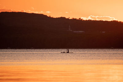 Silhouette person in sea against sky during sunset