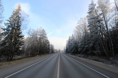 Road amidst trees against cloudy sky