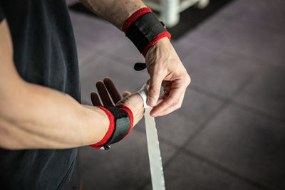 High angle of crop anonymous male athlete taping fingers before weightlifting workout in gym