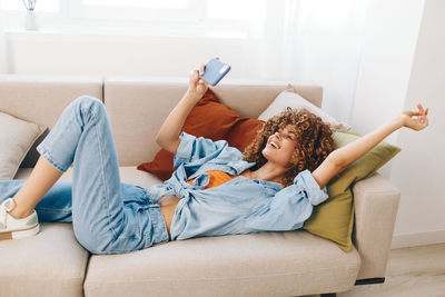 Young woman using phone while lying on sofa at home