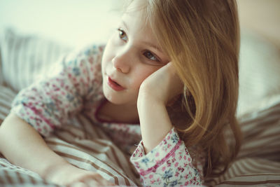 Close-up of cute girl looking away while lying on bed