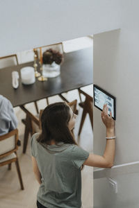 Rear view of girl using digital tablet mounted on wall by brother at modern home