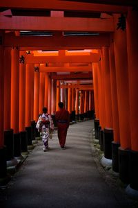 Rear view of man and woman walking under torii gate