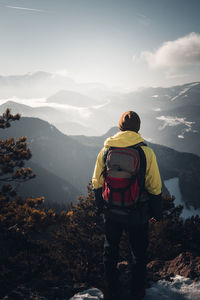 Rear view of man standing on mountain against sky