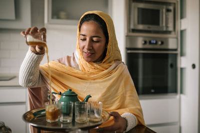 Young woman pouring tea in cup at home