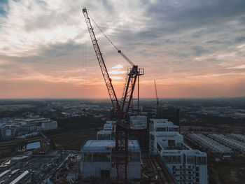 High angle view of cranes and buildings against sky during sunset