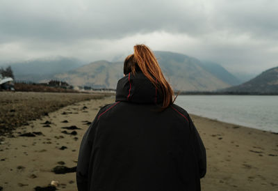 Rear view of woman standing at beach against sky