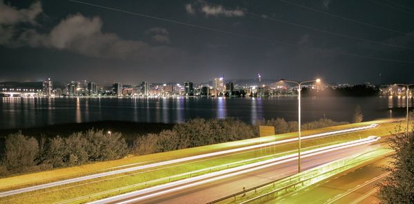 Illuminated city by river against sky at night