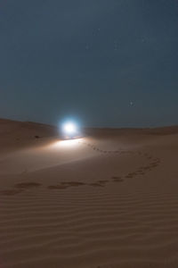 Solo traveler walking in desert holding light source at night under orion.