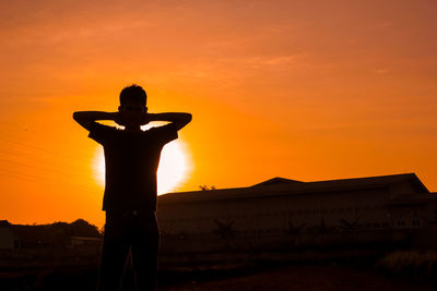 Silhouette man standing on field against orange sky