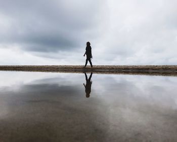 Side view of woman walking at beach against sky
