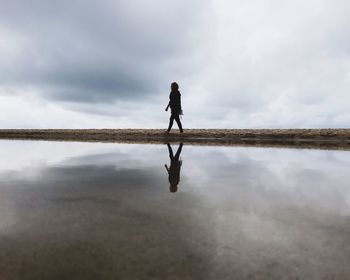 Man walking on beach against sky