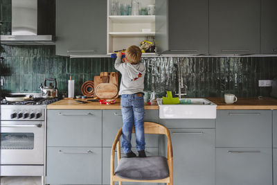 Boy searching in kitchen cabinet standing on chair at home