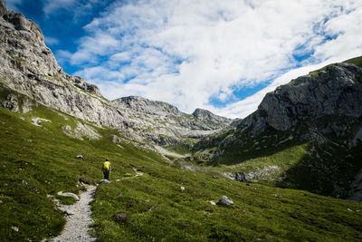 Rear view of woman with backpack standing on mountain against cloudy sky