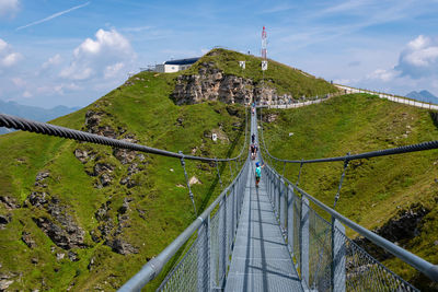 Footbridge over mountain against blue sky during sunny day