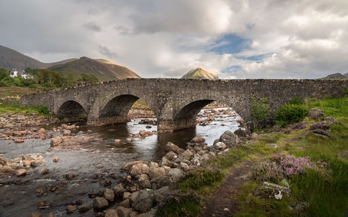 Old stone arch bridge over a river at sligachan on the isle of skye, cuillin mountains rising behind