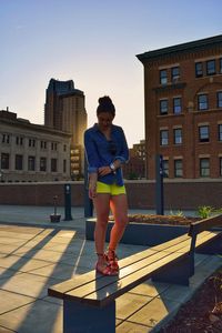 Beautiful woman standing on bench against sky