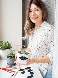 Smiling woman shows handmade decorations for halloween. diy flags and boo sticker on flowerpot.